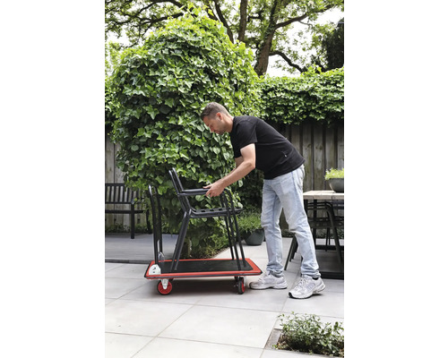 Un homme transporte des chaises sur une planche à roulettes dans le jardin
