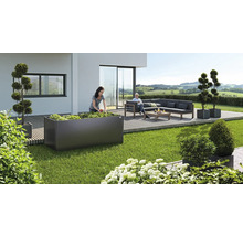 Scène de jardin avec une femme plantant un potager surélevé, un coin salon et des bacs à plantes décoratifs sur une terrasse.