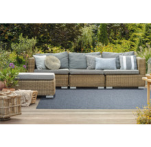 Scène de jardin avec canapé en rotin, coussins et décoration de jardin sur la terrasse devant le jardin