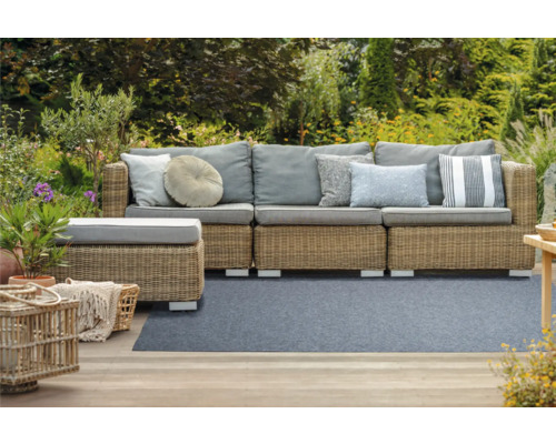 Scène de jardin avec canapé en rotin, coussins et décoration de jardin sur la terrasse devant le jardin