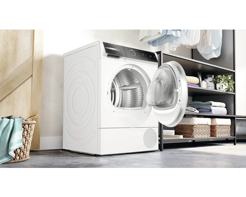 Weisser Wäschetrockner mit geöffneter Tür in einem Waschraum.