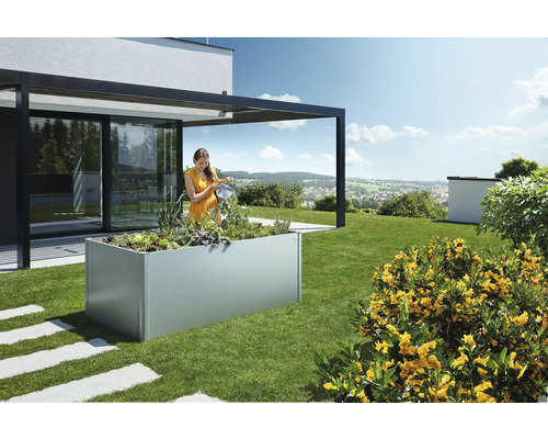 Femme arrosant des plantes dans une jardinière surélevée dans le jardin à côté d''une maison.