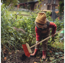 Kind kehrt im Garten mit einem Strassenbesen