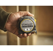 Une main tient un mètre à ruban Stanley Fatmax d''une longueur de huit mètres