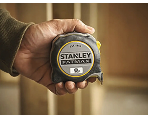 Une main tient un mètre à ruban Stanley Fatmax d''une longueur de huit mètres