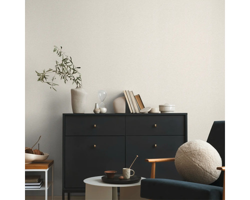 Wohnzimmer mit Kommode, Stuhl und Dekorationsgegenständen vor einer hellen gemusterten Tapete