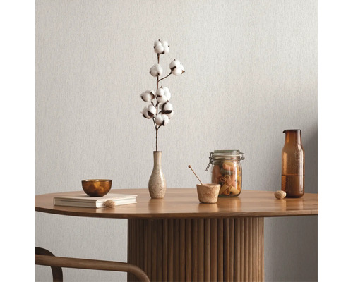Décoration de table avec branche de coton, bol, livre, pot de conservation et bouteille sur une table en bois devant un mur uni.