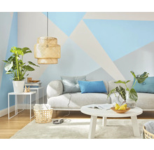 Wohnzimmer mit Sofa, Tisch, Lampe und Zimmerpflanzen vor einer Wand mit geometrischen Mustern