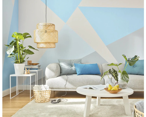 Salon avec canapé, table, lampe et plantes d'intérieur devant un mur aux motifs géométriques