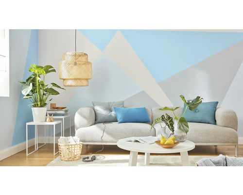 Salon avec canapé, table, lampe et plantes d'intérieur devant un mur aux motifs géométriques