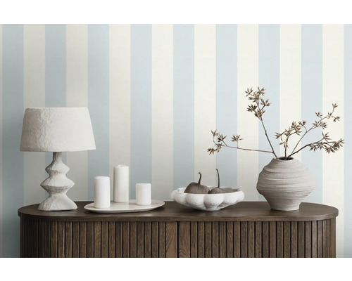 Dekoratives Zimmer mit gestreifter Tapete, Tischleuchte, Kerzen, Schale und Vase auf einem Schrank
