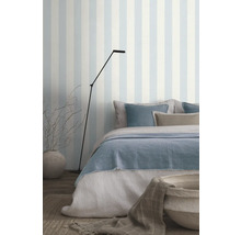 Chambre avec lit, lampadaire et papier peint rayé pour une ambiance lumineuse.