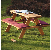 Table de pique-nique en bois avec coussins d'assise, livre et jouet sur la pelouse