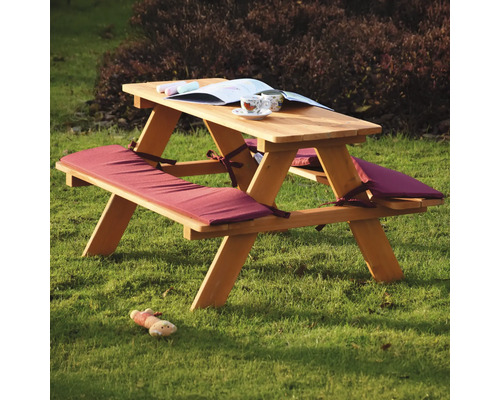 Picknicktisch aus Holz mit Sitzkissen, Buch und Spielzeug auf dem Rasen