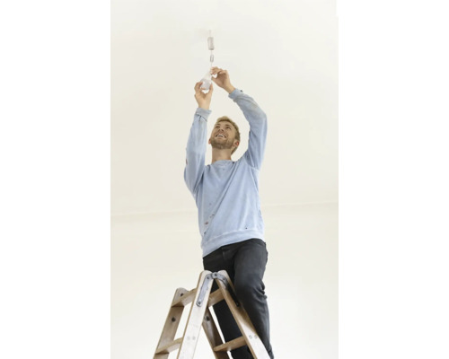 Un homme sur une échelle visse une ampoule dans un plafonnier.