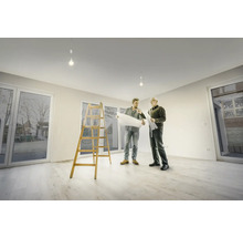 Deux hommes regardent des plans dans une pièce lumineuse avec une échelle et des fenêtres.