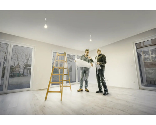 Deux hommes regardent des plans dans une pièce lumineuse avec une échelle et des fenêtres.