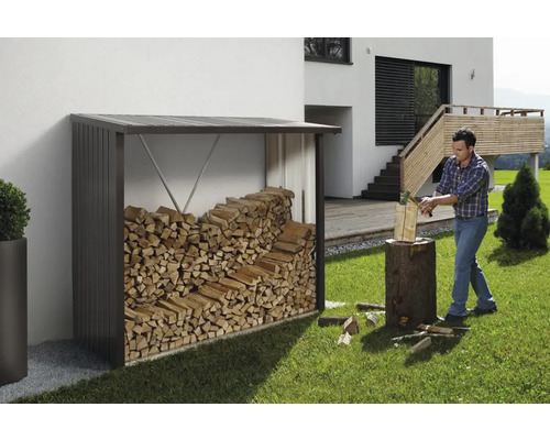 Abri à bois avec bois de chauffage et homme fendant du bois dans le jardin.