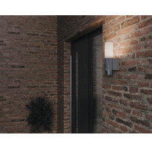 Aussenwandleuchte mit Bewegungsmelder an einer Ziegelmauer neben einer Tür.