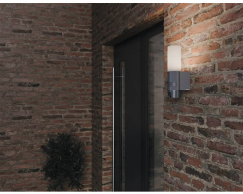 Aussenwandleuchte mit Bewegungsmelder an einer Ziegelmauer neben einer Tür.