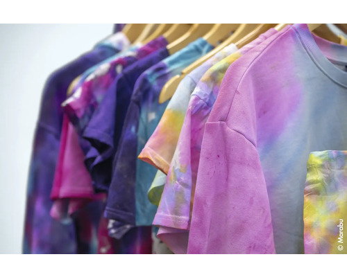 Mehrfarbige T-Shirts mit Batikmuster hängen auf einer Kleiderstange.