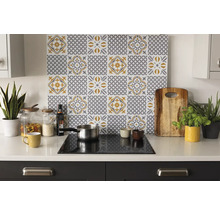 Organisierte helle Küche mit einer Rückwand mit grau-gelbem Fliesenmuster hinter einem Kochfeld auf weisser Arbeitsplatte mit Utensilien und Pflanzen.