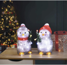 Zwei Pinguinfiguren mit Beleuchtung und Weihnachtsmotiv auf einem Tisch vor einem Weihnachtsbaum.