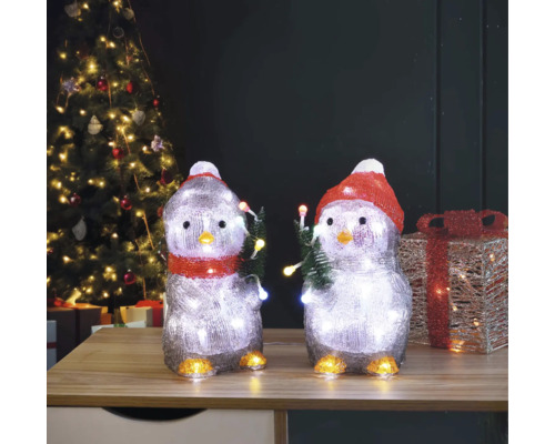 Zwei Pinguinfiguren mit Beleuchtung und Weihnachtsmotiv auf einem Tisch vor einem Weihnachtsbaum.