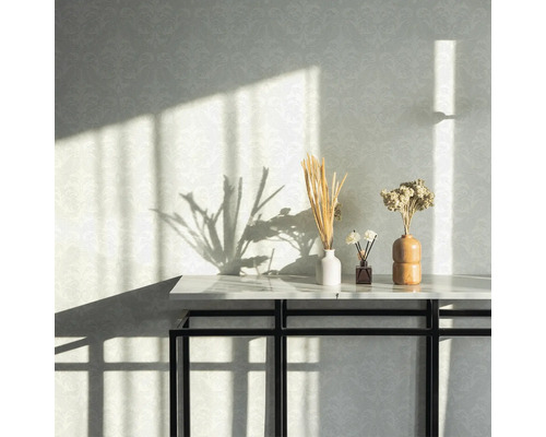 Dekorative Elemente auf einem Tisch vor einer gemusterten Wand mit Sonnenlicht.