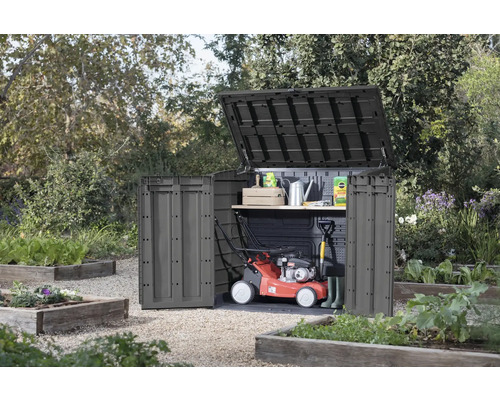 Armoire de jardin avec couvercle et porte ouverts dans le jardin, avec tondeuse à gazon et outils de jardinage