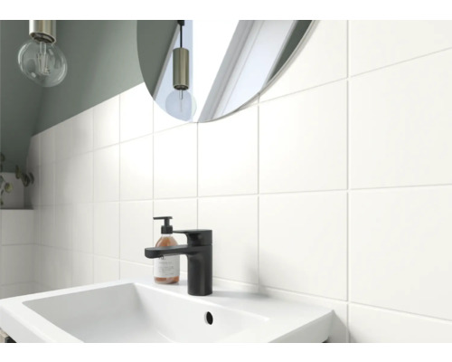 Lavabo de salle de bain avec robinet, distributeur de savon et miroir devant un mur carrelé