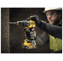 Un homme perce un trou dans un mur avec une perceuse-visseuse sans fil DeWalt.