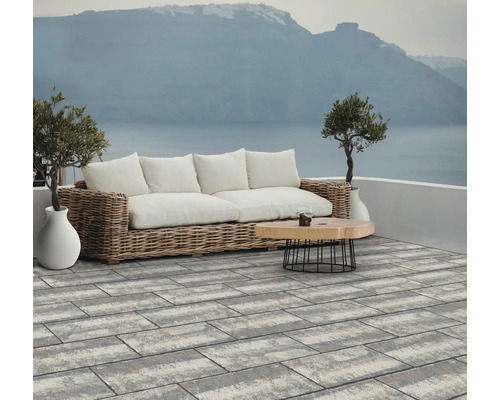 Terrasse mit Rattansofa, Holztisch und Pflastersteinen