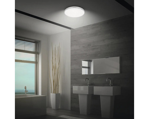 Badezimmer mit runder Deckenleuchte, zwei Waschbecken und Badewanne am Fenster.