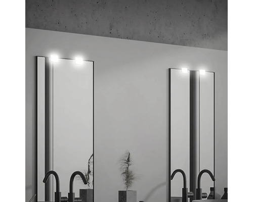 Zwei beleuchtete Spiegel mit Armaturen in einem Badezimmer.