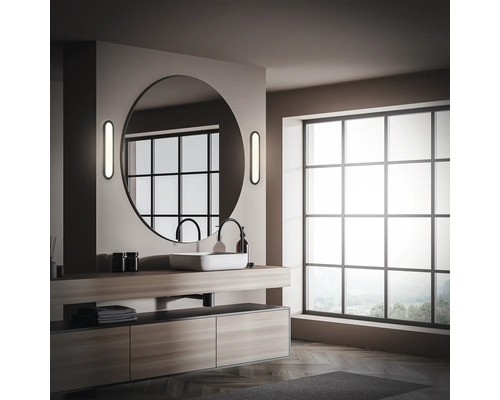 Badezimmer mit Waschtisch, rundem Spiegel und großem Fenster