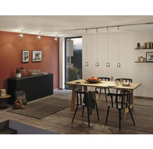 Salle à manger avec table en bois, chaises noires, commode et système d'éclairage