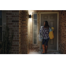 Szene mit einer Frau, die vor einer Haustür unter einer Wandleuchte steht