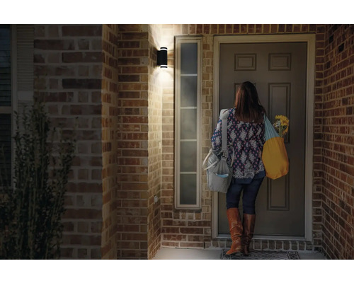 Szene mit einer Frau, die vor einer Haustür unter einer Wandleuchte steht