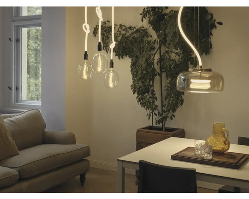 Esszimmer mit Sofa, Esstisch, Zimmerpflanze und verschiedenen Pendelleuchten.