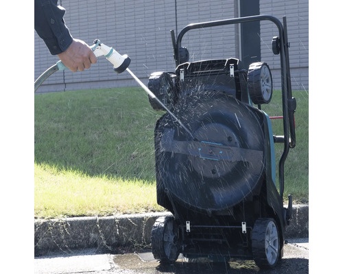 Une tondeuse à gazon est nettoyée avec un tuyau d'arrosage.