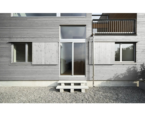 Fassade eines Hauses mit Holzverkleidung, Fenstern, Schiebeläden und Eingangstür