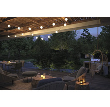 Terrasse décorée avec des meubles de salon, des guirlandes lumineuses et une végétation luxuriante pour une atmosphère détendue.