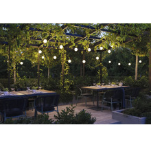Pergola éclairée avec tables à manger et chaises dans un jardin.