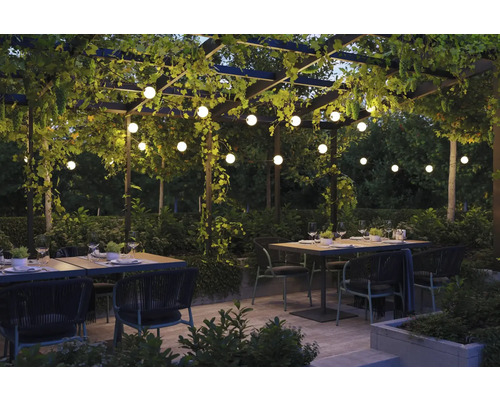 Pergola éclairée avec tables à manger et chaises dans un jardin.