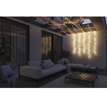 Terrasse éclairée avec guirlandes lumineuses, canapé et table basse.