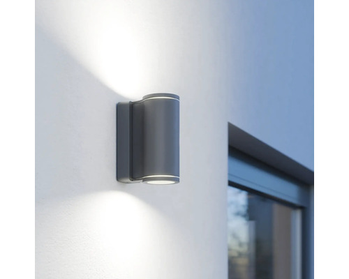 Graue LED-Aussenwandleuchte mit zylindrischem Design an einer Wand