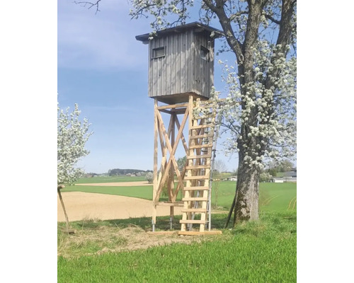 Hochsitz aus Holz auf einer Wiese mit Feldern im Hintergrund