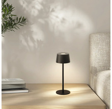 Schwarze Tischleuchte auf einem Nachttisch mit Büchern und einem Bett im Hintergrund