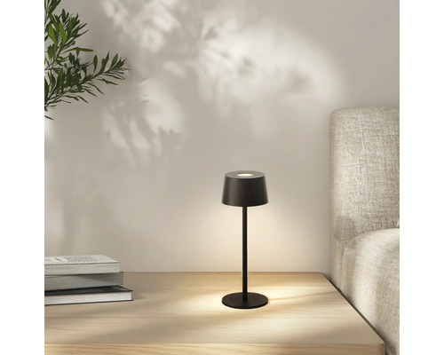 Schwarze Tischleuchte auf einem Nachttisch mit Büchern und einem Bett im Hintergrund